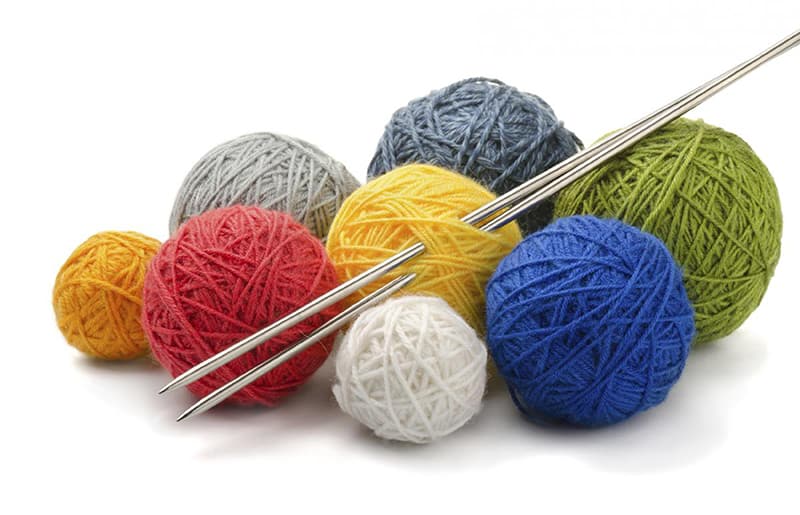 photo of knitting needles with eight balls of coloured wool