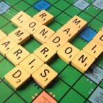 A green Scrabble board with city names spelled out on it.