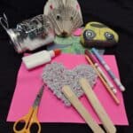 A display of many crafted items. There is a hedgehog made from book pages and a rock painted to look like a car. There are craft supplies scattered on the table.