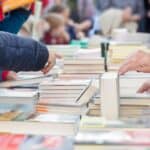 A table absolutely filled with books. People surround the table and pick through the available books.