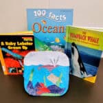 A paper craft scenery of underwater creatures. Behind the scene are children's books about oceans and ocean animals.