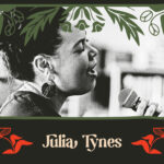 A black and white photo of Julia Tynes. She is a black woman with dark curly hair tied in a bun. She sings passionately into a microphone.