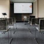 A room lined with metal chairs. At the back of the room is a projector screen with a presentation being shown.